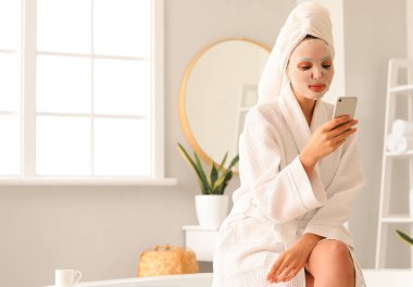 Banyoda cep telefonu kullanan, çarşaf maskeli genç bir kadın.