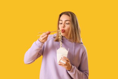 Sarı arka planda Çin eriştesi yiyen genç bir kadın.