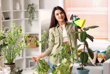 Evde sprey şişesi ve yeşil çiçekleri olan genç bir kadın var.