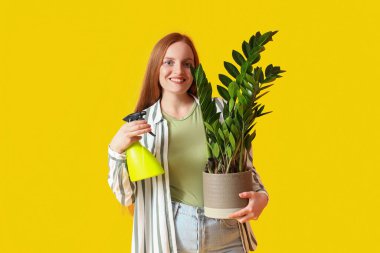 Sarı arka planda yeşil çiçekli sprey şişeli genç bir kadın.