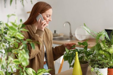 Evde yeşil çiçekli genç bir kadın cep telefonuyla konuşuyor.