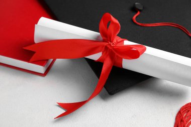 Diploması kırmızı kurdeleli ve mezuniyet şapkası beyaz masada.