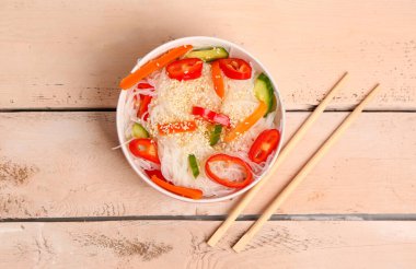 Lezzetli pirinç erişteleri, yemek çubukları ve sebzelerle dolu bir kase.