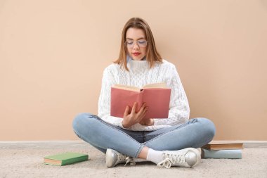 Bej duvarın yanında kitap okuyan genç bir kadın.