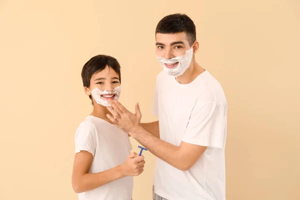 Father and his little son shaving against beige background