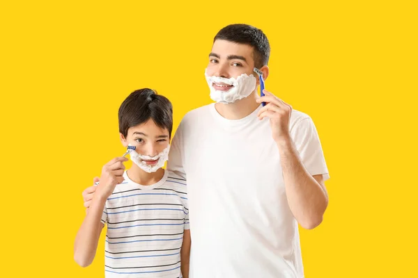 Man and his little son shaving against yellow background