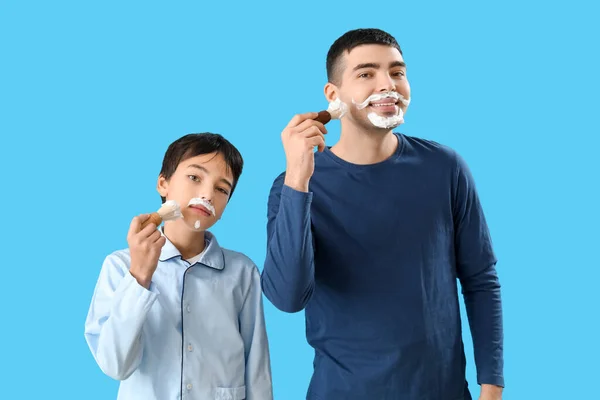 Homem Seu Filho Aplicando Espuma Barbear Rostos Contra Fundo Azul — Fotografia de Stock