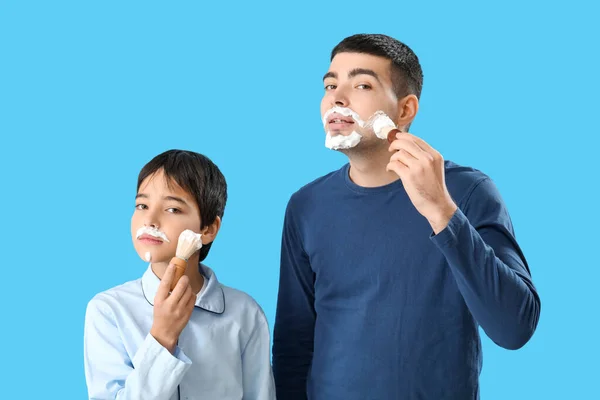 Homem Seu Filho Aplicando Espuma Barbear Rostos Contra Fundo Azul — Fotografia de Stock