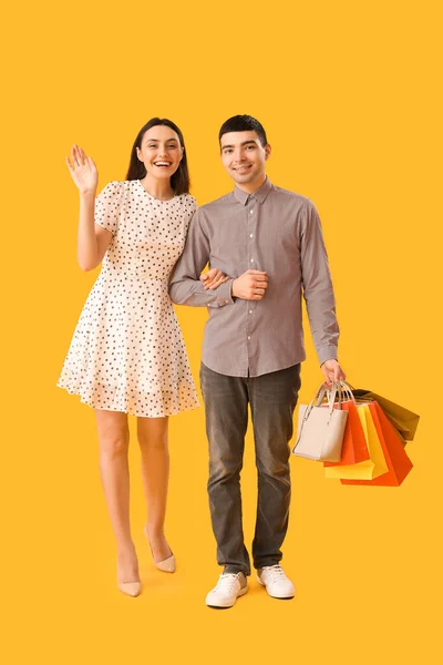 可爱的年轻夫妇 手牵手提着购物袋走在黄色的背景上 — 图库照片