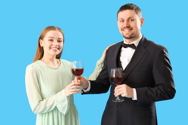 Young man in suit giving his wife glass of wine on blue background