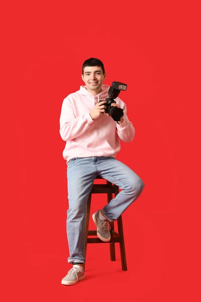 Jovem Fotógrafo Masculino Com Câmera Profissional Sentado Fundo Vermelho — Fotografia de Stock