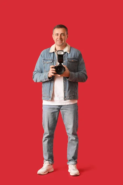 Mature photographer with professional camera on red background