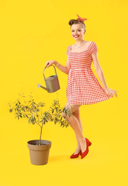 黄色の背景に散水缶と観葉植物を持つ若いピンアップ女性 — ストック写真
