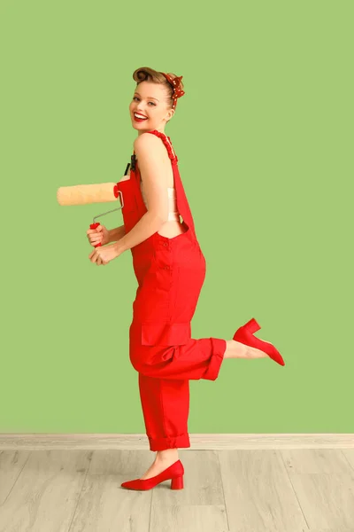 緑の壁の近くに塗料ローラーと赤の制服の若いピンアップ女性 — ストック写真