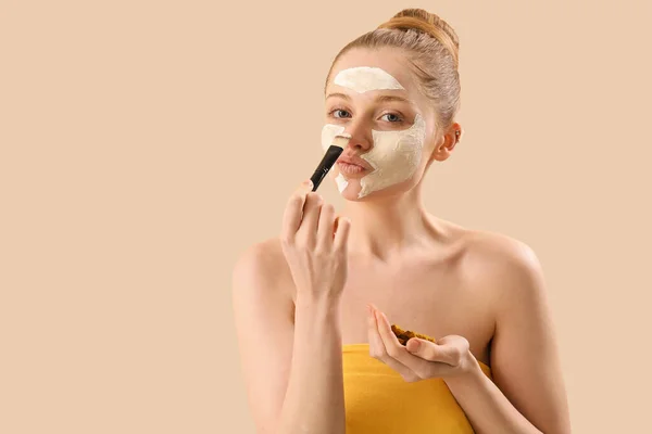 適用ターメリックマスクを持つ若い女性 ベージュの背景にブラシと根 — ストック写真