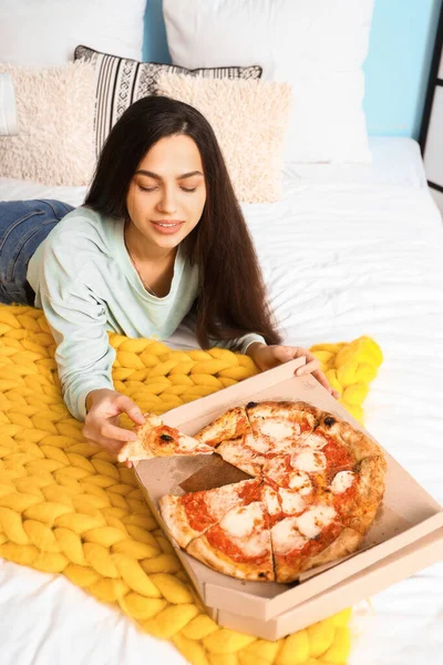 在卧室里躺着一个带着美味披萨的年轻女人 — 图库照片