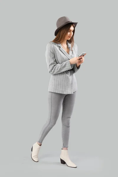 灰色の背景にスマートフォンを持つスタイリッシュな若い女性 — ストック写真