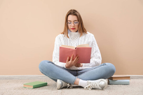 Young woman reading book near beige wall