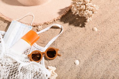 İçinde güneş kremi, tıbbi maske, güneş gözlüğü, kumda şapka ve mercan olan bir çanta. Melanoma kavramı