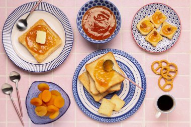 Lezzetli tost tabakları, kayısı reçeli ve pembe fayanslı bir fincan kahve.