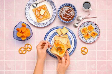 Kadın pembe fayanslı kayısı reçelli lezzetli tostlar hazırlıyor.