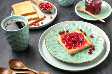 Kızılcık reçelli lezzetli tost ve koyu arkaplanda bir fincan kahve.