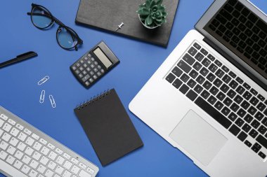 Mavi arkaplanda dizüstü bilgisayar, gözlük ve hesap makinesi ile kompozisyon