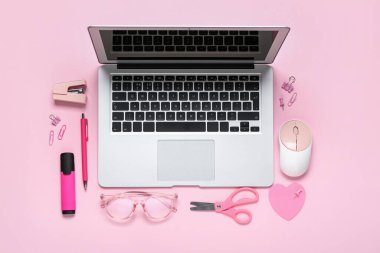 Pembe arka planda dizüstü bilgisayar, kırtasiye ve gözlüklü kompozisyon