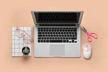 Bej arkaplanda dizüstü bilgisayar, gözlük ve makas bileşimi