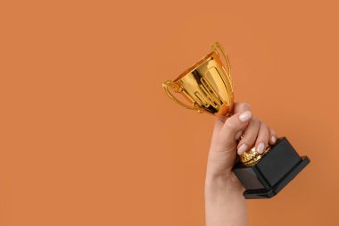 Turuncu arka planda altın bardaklı kadın.