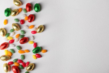 Folyo içinde çikolatalı Paskalya yumurtaları ve gri masada şekerler.