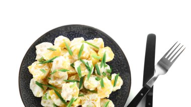 Beyaz arka planda yeşillikleri olan lezzetli patates salatası tabağı.