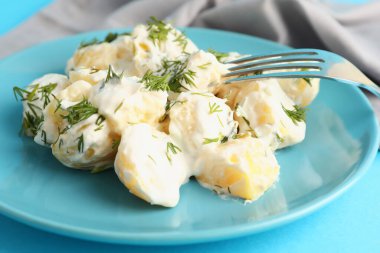 Bir tabak lezzetli patates salatası. Mavi arka planda yeşiller, yakın plan.