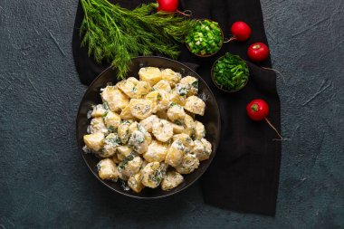 Koyu arkaplanda yeşillikler olan bir kase lezzetli patates salatası.