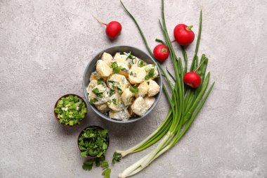 Bir kase lezzetli patates salatası ve gri arka planda yeşiller.