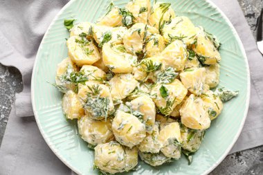 Bir tabak lezzetli patates salatası ve arkaplanda yeşillikler.