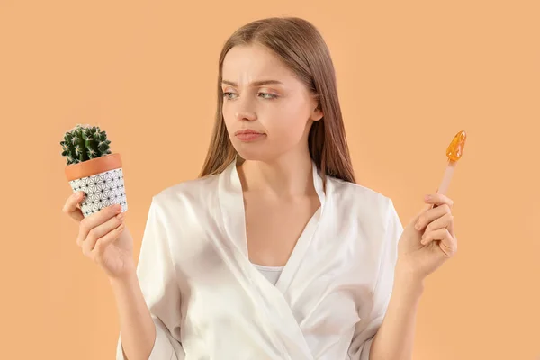 Displeased young woman with sugaring paste and cactus on beige background