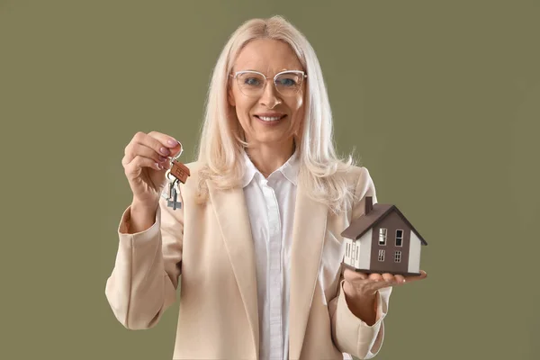 Mature real estate agent with keys and house model on green background
