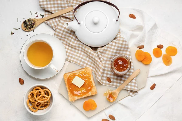 stock image Tasty toast with apricot jam, cookies and cup of tea on light background