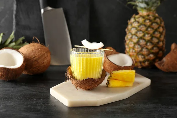 stock image Board with glass of tasty pineapple smoothie and coconut on black grunge table