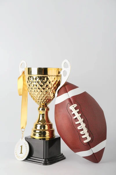 Gold cup with first place medal and rugby ball on light background