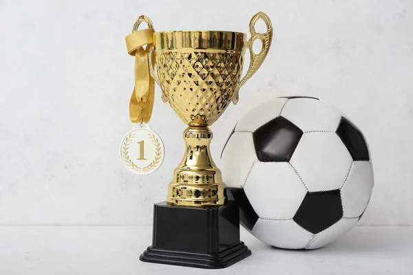 Gold cup with first place medal and soccer ball on light background