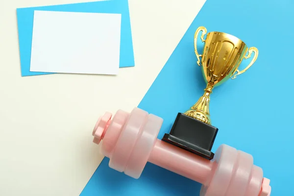Blank card with gold cup and dumbbell on color background