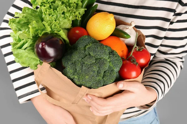 灰色の背景に野菜や果物を入れた紙袋を持った女性 — ストック写真
