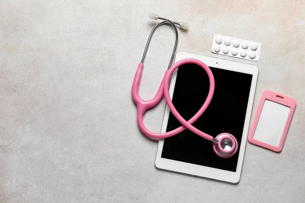 Stethoscope, tablet computer, badge and pills on light background