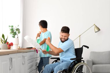 Küçük çocuk ve babası tekerlekli sandalyede temizlik yaparken eğleniyorlar.