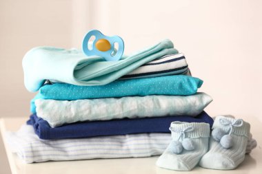 Bebek kıyafetleri ve emzik yığını odadaki masada, yakın plan.