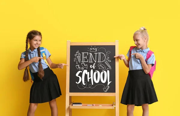 Cute students near chalkboard with text END OF SCHOOL on yellow background