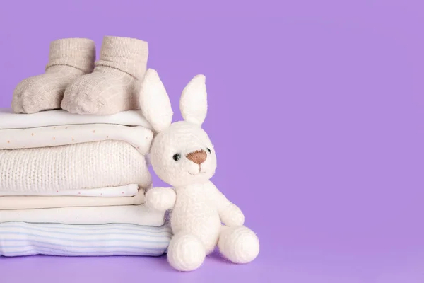 stock image Stack of baby clothes, socks and knitted toy on lilac background