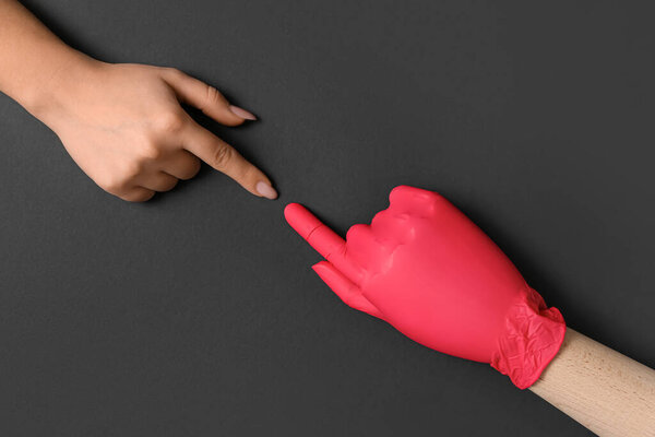 Woman and wooden hand in rubber glove on black background